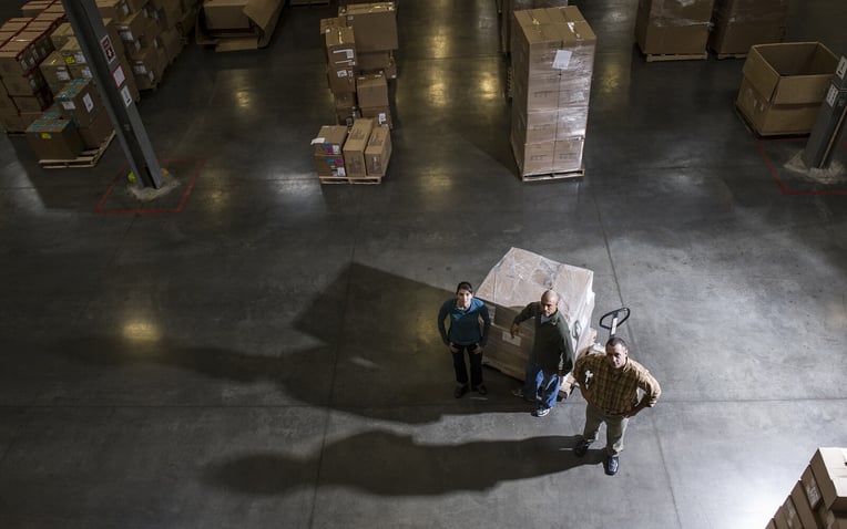 A group of three warehouse workers standing in the center of a distribution warehouse.