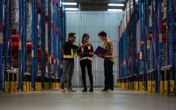 Three warehouse workers use a handheld OMS portal to evaluate their 3PL storage rates while on the floor.