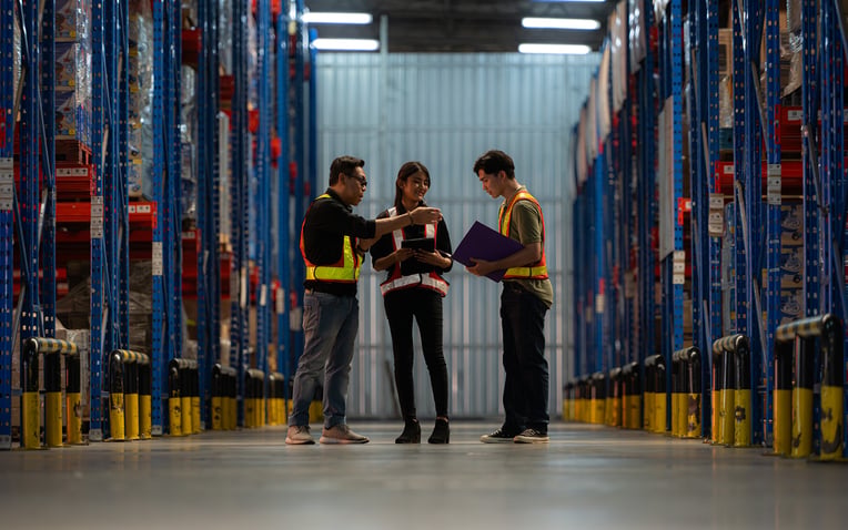 Three warehouse workers use a handheld OMS portal to evaluate their 3PL storage rates while on the floor.