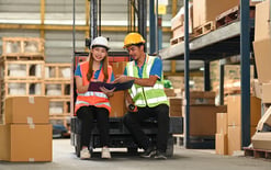Warehouse workers sitting on forklift truck discussing the advantages and disadvantages of 3PLs