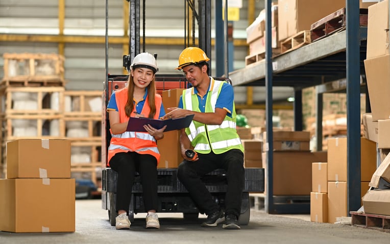 Warehouse workers sitting on forklift truck discussing the advantages and disadvantages of 3PLs