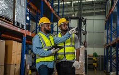 Two warehouse workers practice efficient apparel fulfillment by consulting their WMS before picking an order off the shelves
