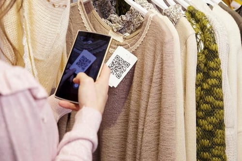 woman scanning QR code on sweater in retail store